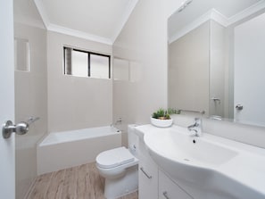 Een moderne badkamer met een badkuip, toilet, wastafel en een raam boven het toilet.