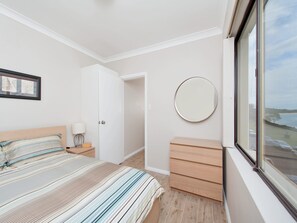 Ein Schlafzimmer mit Bett, Nachttisch, Lampe, Kommode und einem runden Spiegel.