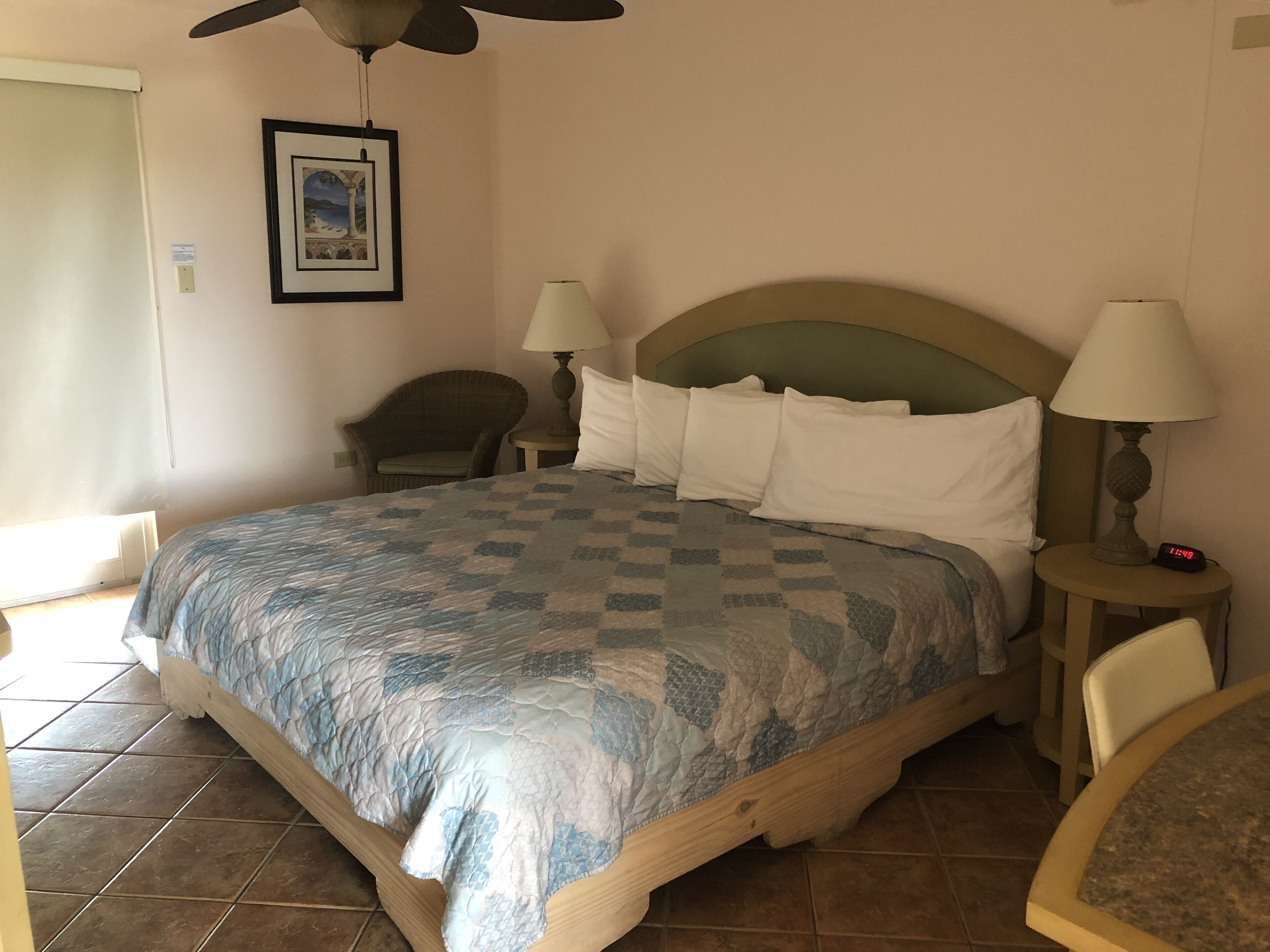 A hotel room with a bed, two bedside lamps, a chair, a ceiling fan, and a framed picture on the wall.
