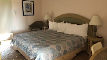 A hotel room with a bed, two bedside lamps, a chair, a ceiling fan, and a framed picture on the wall.