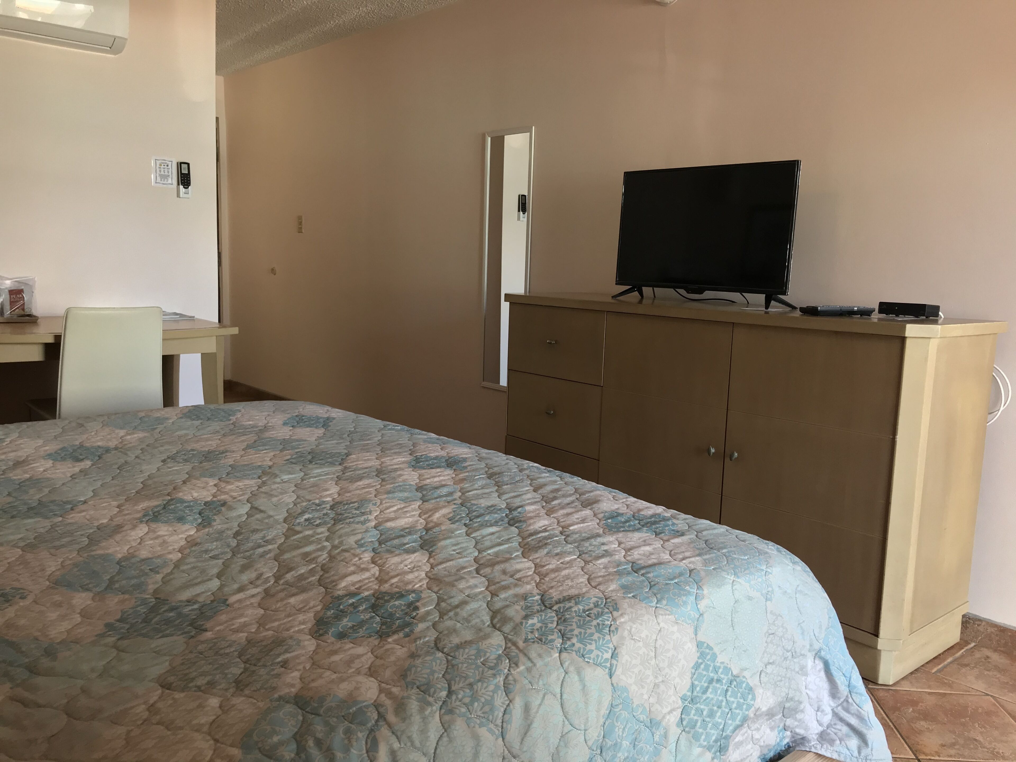 Un dormitorio con cama, escritorio, televisor sobre un mueble y una puerta.