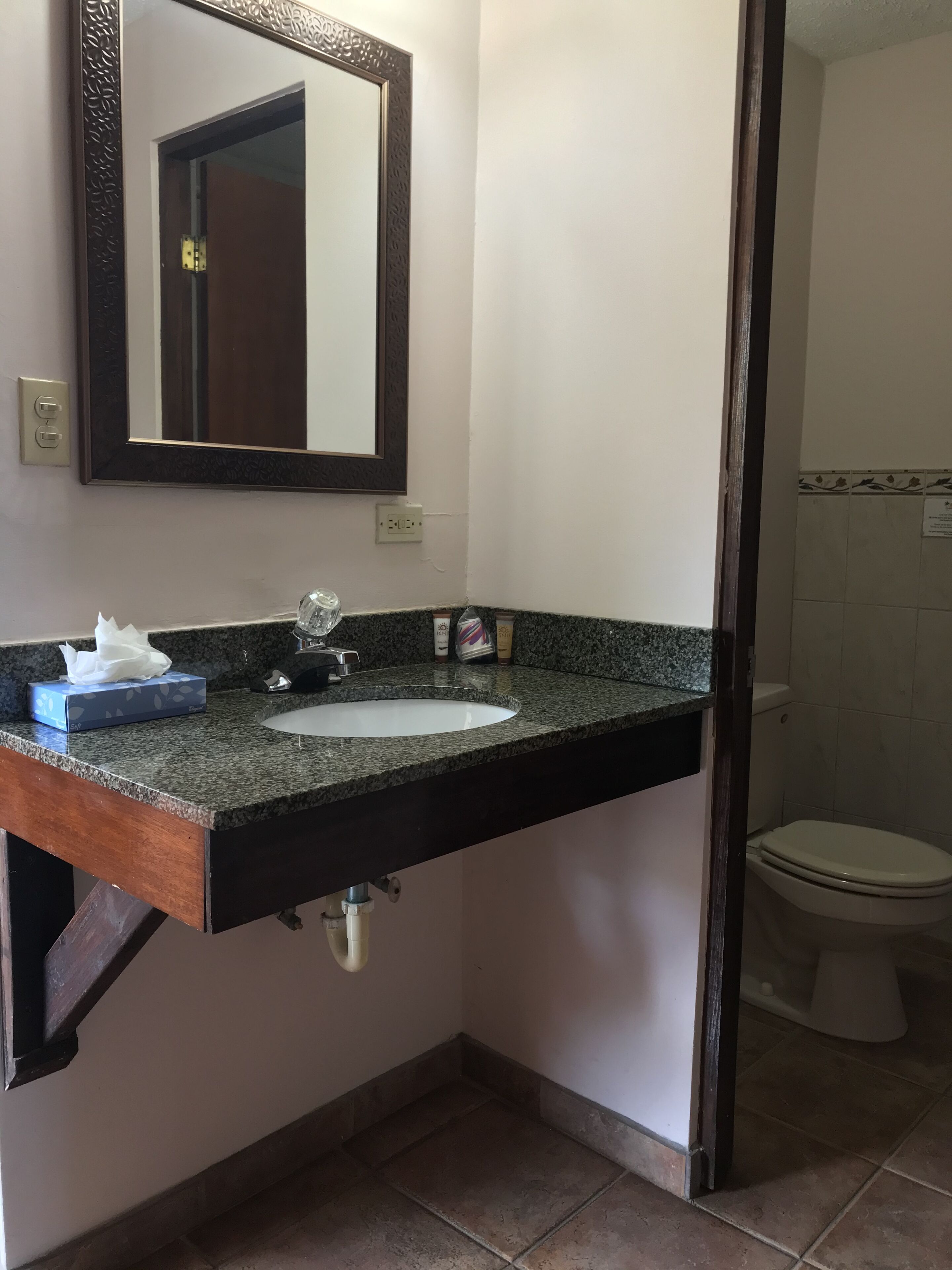 Ein Badezimmer mit einer Granit-Arbeitsplatte, einem weißen Waschbecken, einem Spiegel mit Zierrahmen und einer Toilette.