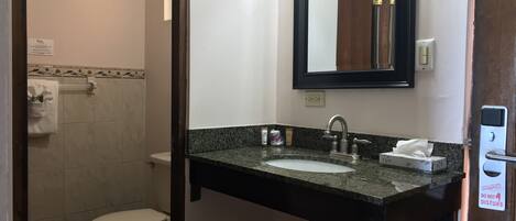 Een badkamer met een marmeren vloer, een wit toilet, een wastafel met granieten blad, een spiegel en een zeepdispenser.
