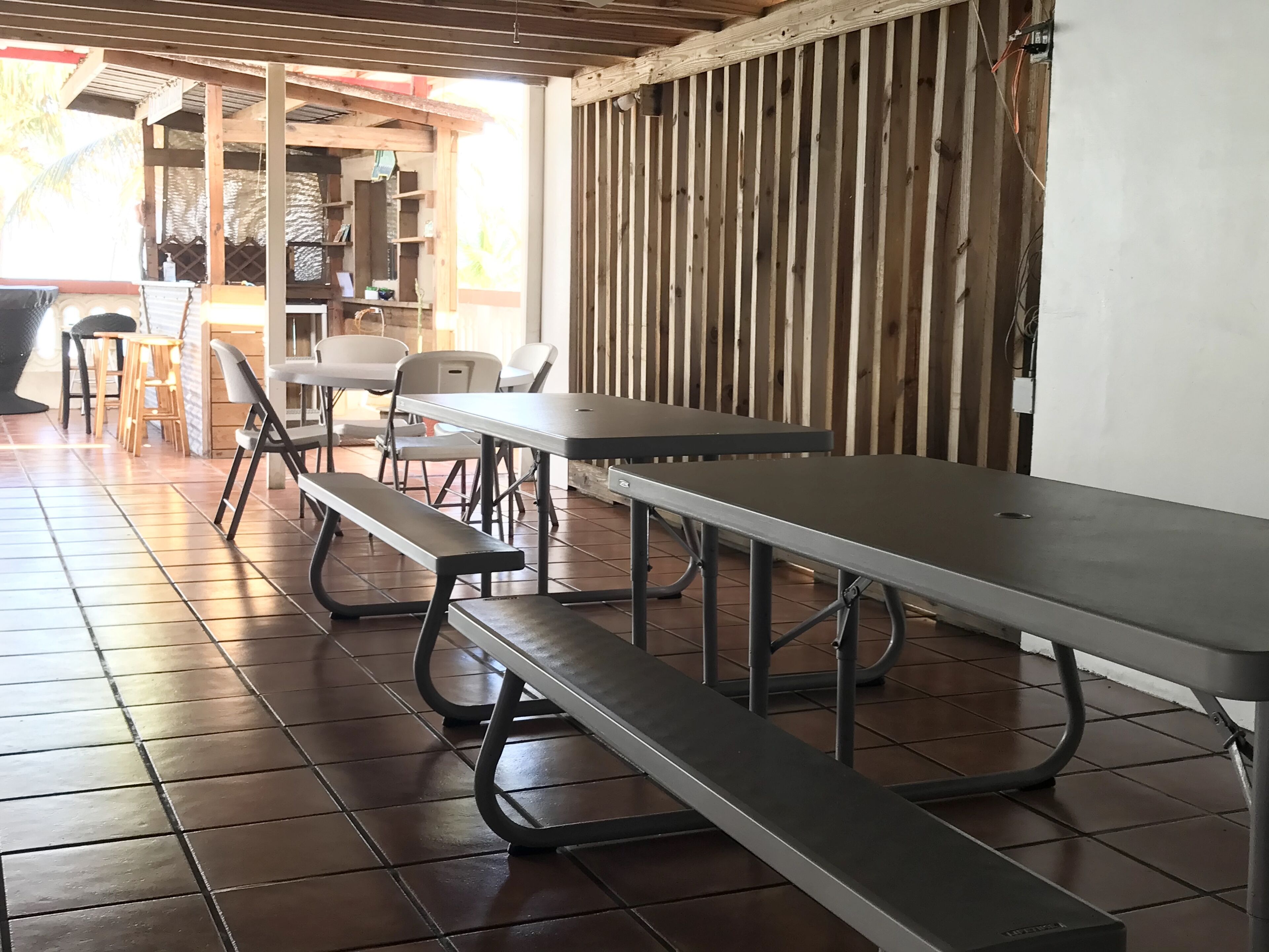 A dining area with metal tables and benches, a tiled floor, and a wooden wall with vertical slats.