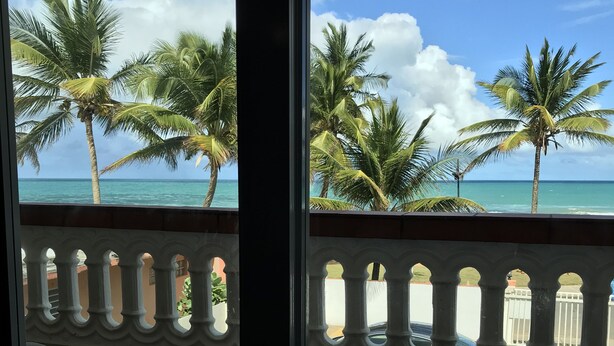 A balcony with a view of the ocean and palm trees. - Luquillo Sunrise beach Inn (Luquillo)