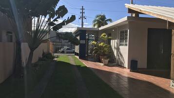 Zona residencial con camino pavimentado, entrada con portón y un pequeño edificio con techo de tejas.