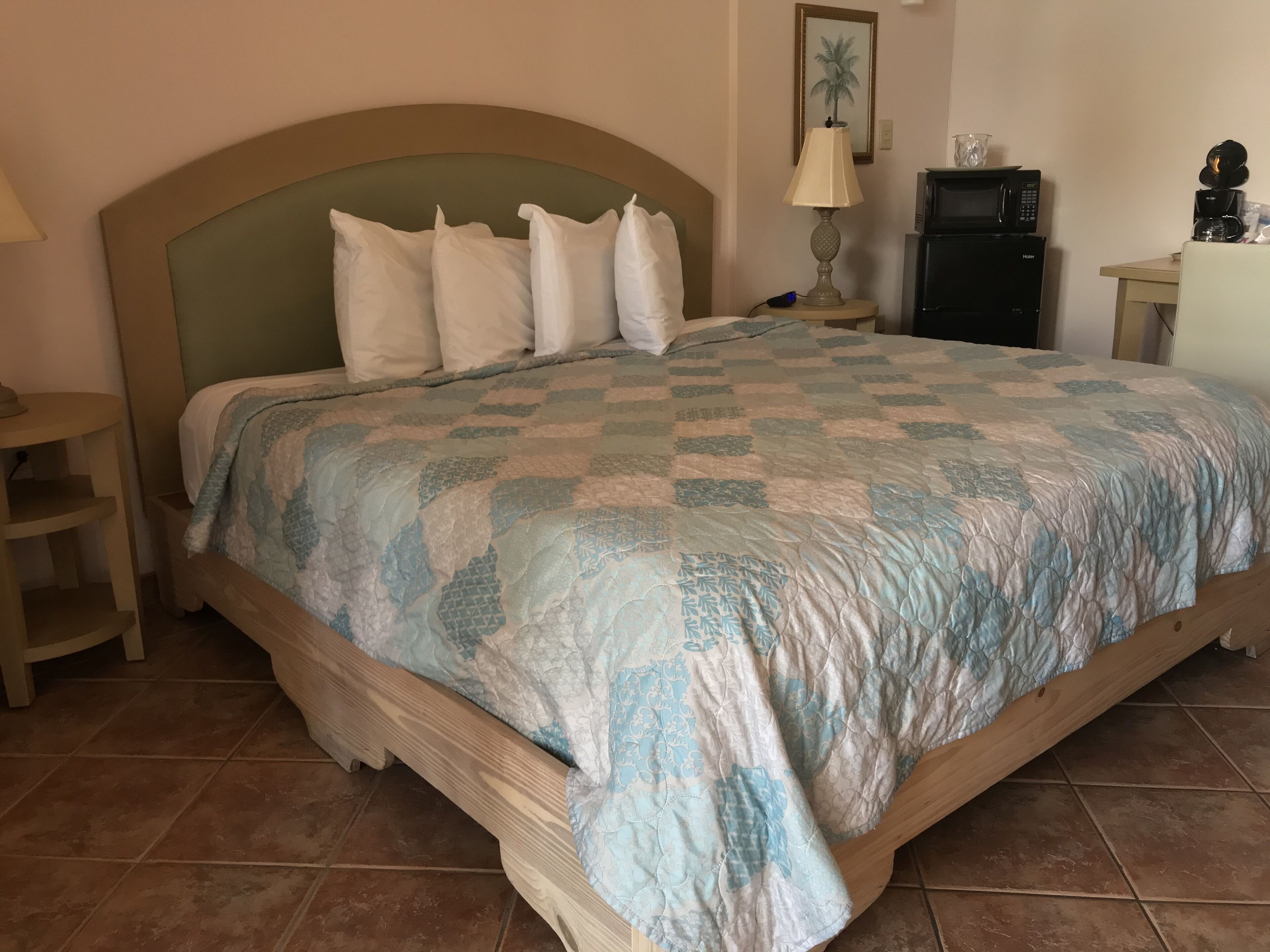 A bedroom with a bed, a nightstand, a lamp, a microwave, and a small table with a coffee maker.