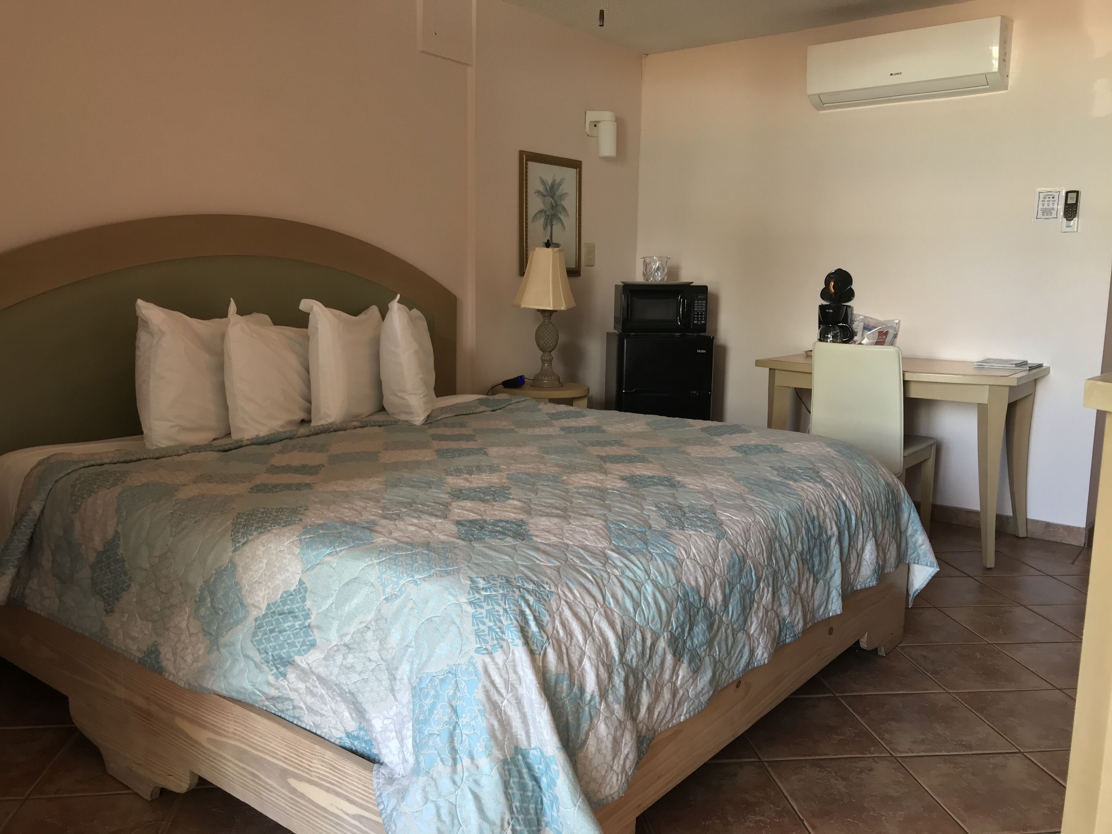 Un dormitorio con cama, escritorio, lámpara, microondas y refrigerador.