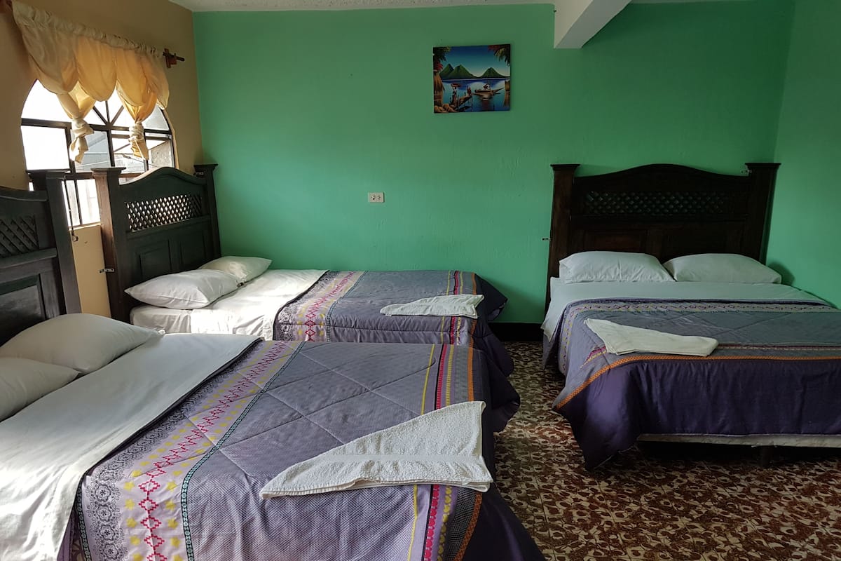 Una habitación con dos camas, cada una con una colcha y almohadas estampadas. Hay una ventana con cortinas, un cuadro en la pared y una alfombra estampada.