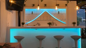 Een bar met een wit aanrecht, drie krukken, een fietsdecoratie en hangende lampen.