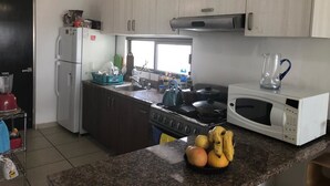 A modern kitchen with white cabinets, a stainless steel refrigerator, a stove, a microwave, and a sink. - Shanghai (Cancun)