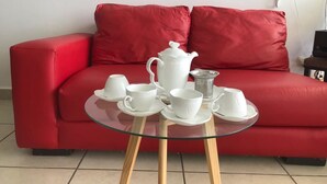 A red sofa with a glass table in front, holding white teacups and a teapot. - Shanghai (Cancun)