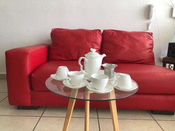 En rød sofa med et glasbord foran, hvor der står hvide tekopper og en tepotte.