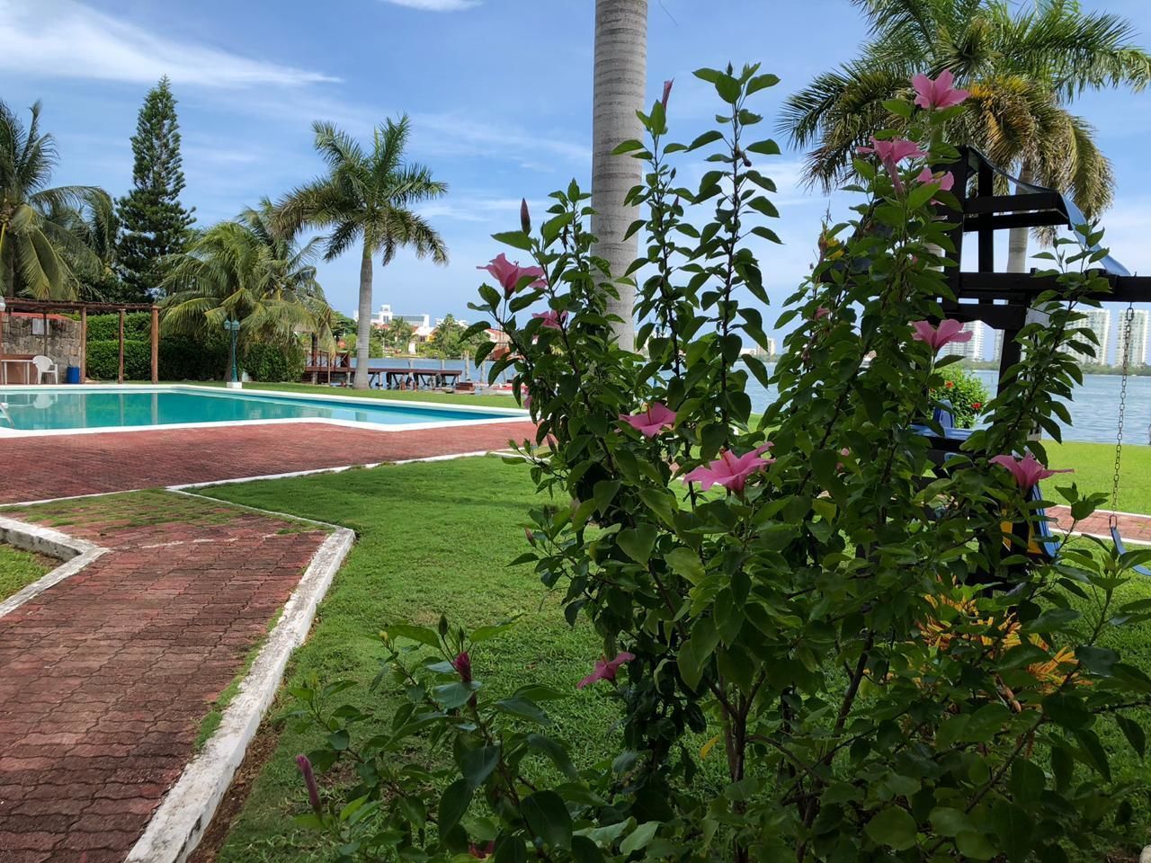 Un área de piscina con un sendero de ladrillo, abundante vegetación y un arenero.