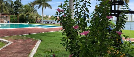 Un área de piscina con un sendero de ladrillo, abundante vegetación y un arenero.