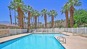 Une piscine bordée de palmiers, avec des chaises longues et une clôture blanche.