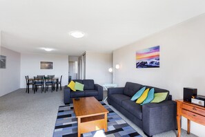 A modern living room with a sofa, coffee table, and a dining area with chairs and a table.
