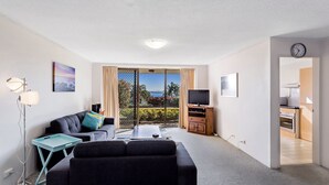 A modern living room with a sofa, TV, and a balcony with a view. - A ground floor unit, close to town (Nelson Bay)