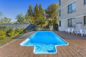 Une piscine rectangulaire bordée de carreaux bleus, entourée d’une terrasse en briques.