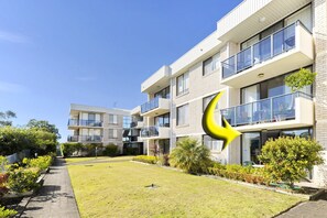 A modern multi-story residential building with balconies and a well-maintained lawn.