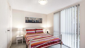 Een slaapkamer met een bed, twee nachtkastjes, een schilderij aan de muur en een raam met jaloezieën.