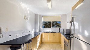 A compact kitchen with a black countertop, wooden cabinets, a stainless steel refrigerator, and a window with a view of trees. - A ground floor unit, close to town (Nelson Bay)