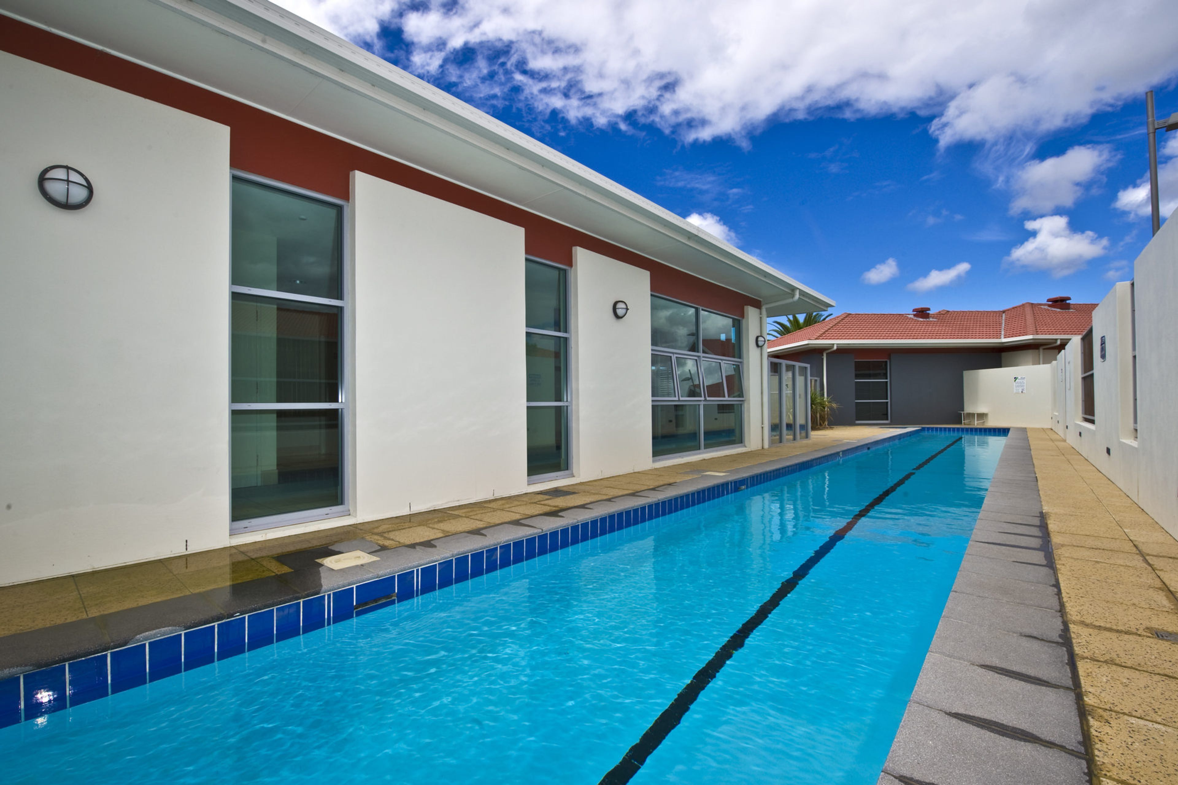 A swimming pool adjacent to a building with large windows and a red roof.