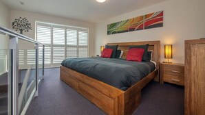 Une chambre à coucher avec un grand lit, une table de chevet, une lampe, une armoire et une rambarde en verre.