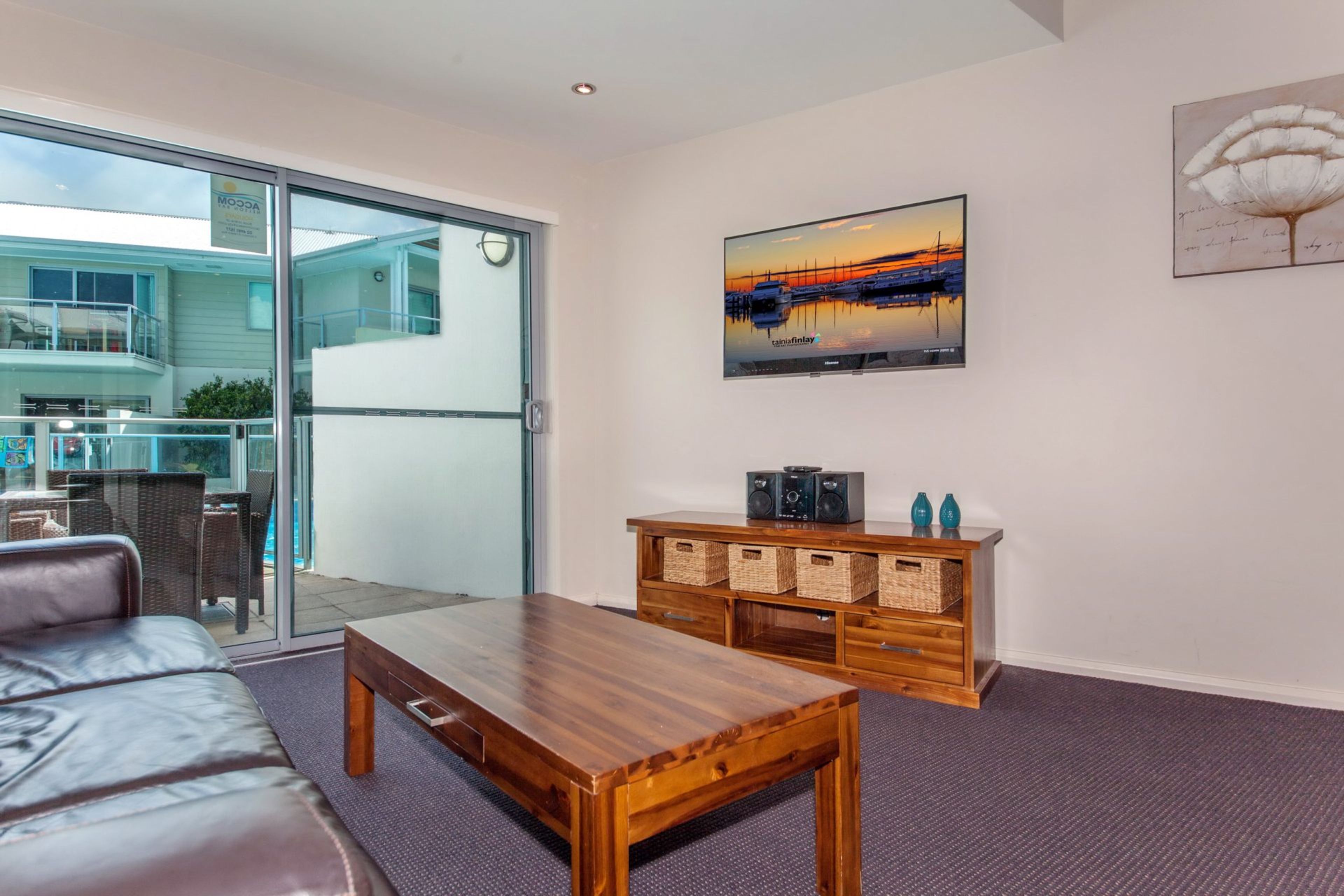 A modern living room with a glass door leading to a balcony, a wooden coffee table, a sofa, and a wall-mounted TV.