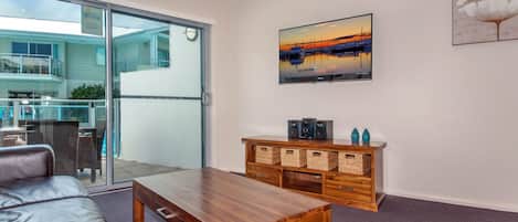 A modern living room with a glass door leading to a balcony, a wooden coffee table, a sofa, and a wall-mounted TV.