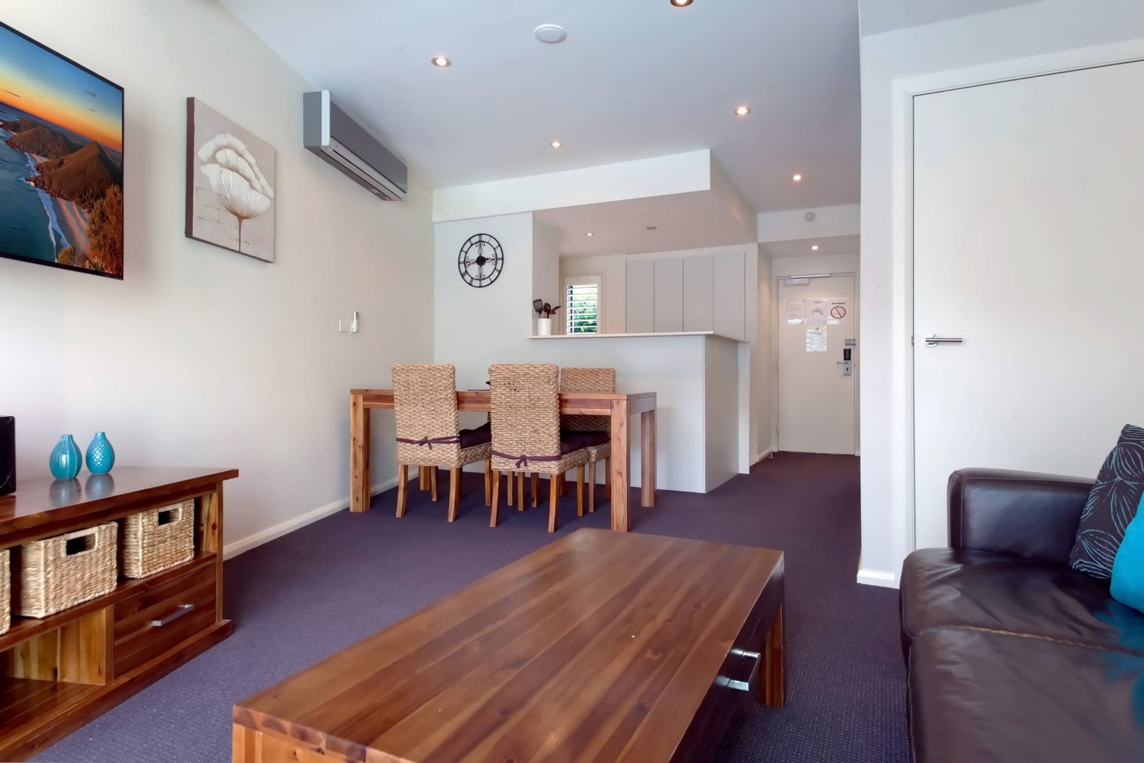 A modern living room with a wooden dining table, wicker chairs, a sofa, and a TV.