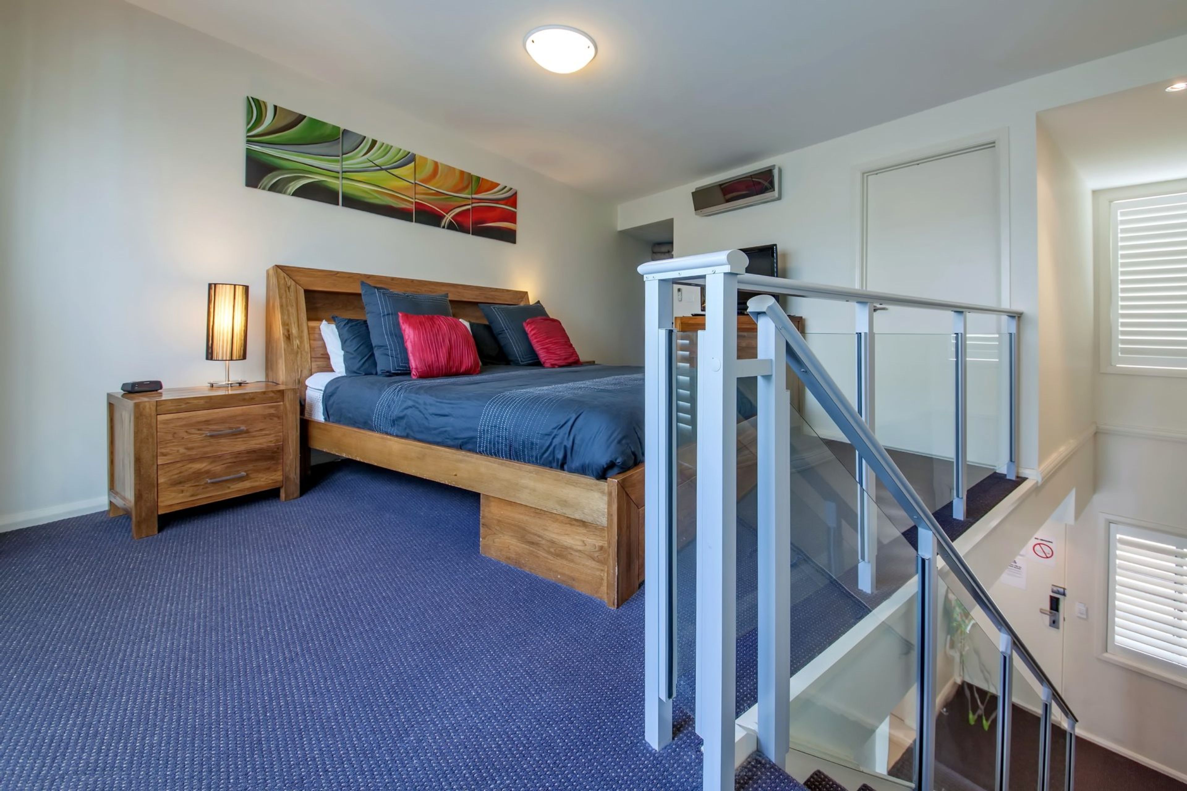 Un dormitorio con cama, mesita de noche, lámpara y un cuadro en la pared.
