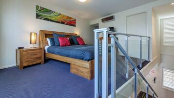 Un dormitorio con cama, mesita de noche, lámpara y un cuadro en la pared.