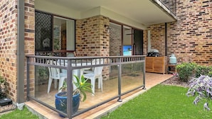 Een glazen balkon met een tafel, stoelen, een barbecue en uitzicht op een strand.
