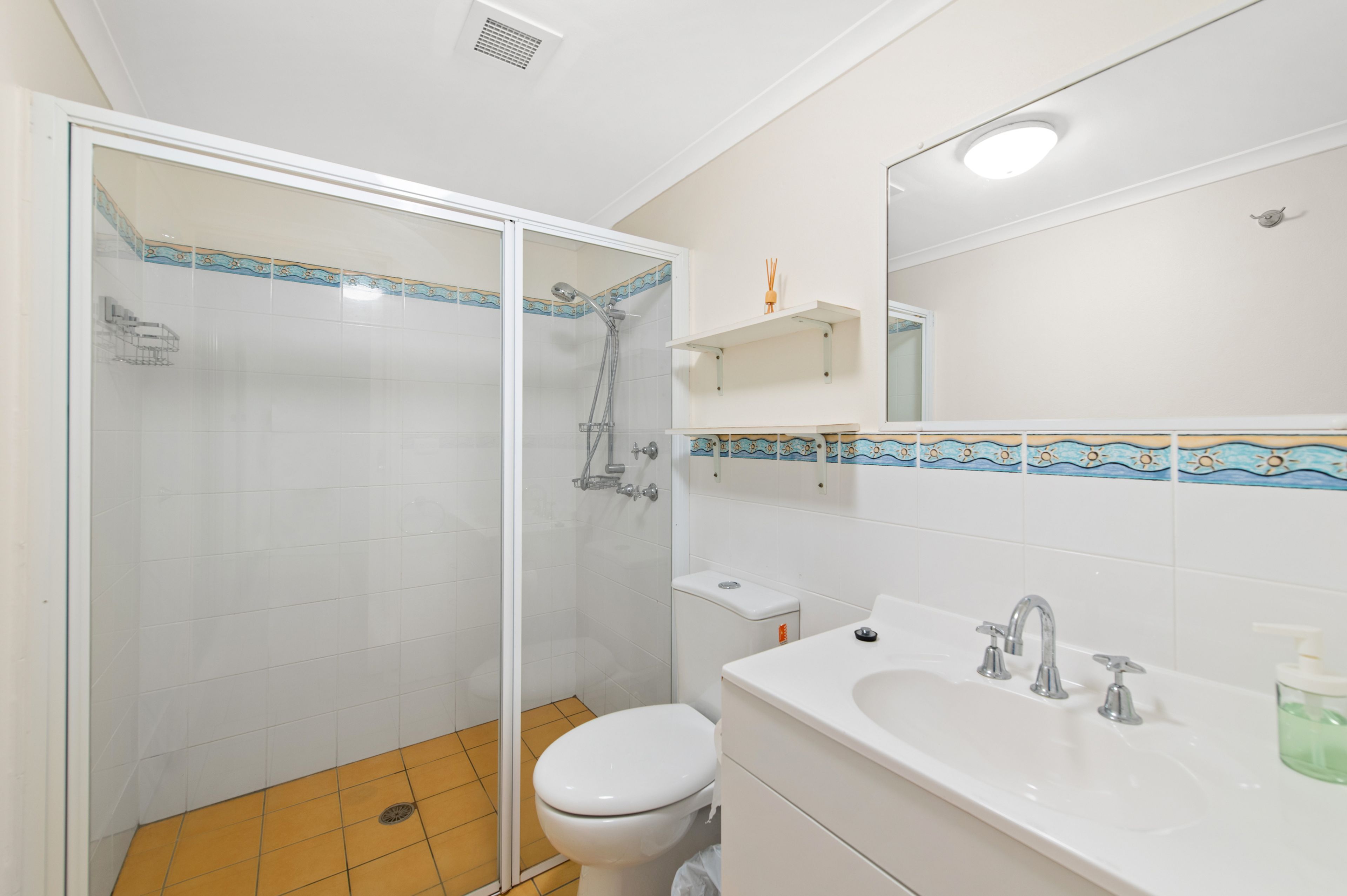 A bathroom with a shower, toilet, sink, and a mirror.
