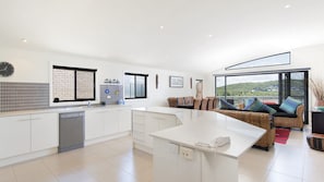 A modern kitchen with a central island, white cabinetry, and a view of a lush landscape through large windows. - Fingal Surf & Sand, 14A Pacific Drive- Modern, 2-storey duplex between bushland and the beach (Fingal Bay)