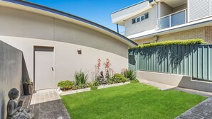 Une maison moderne à la façade incurvée, dotée d’un petit jardin avant avec du gazon synthétique et ornée d’une statue représentant une figure assise.