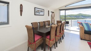 Un coin repas avec une table et des chaises, un tableau encadré au mur et une vue sur un plan d’eau et des collines.