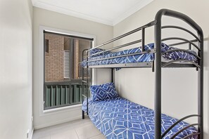 A bunk bed with a geometric patterned bedspread and matching pillows, a window with a view of a brick wall, and a metal ladder. - Fingal Surf and Sand Pet Friendly with views (Fingal Bay)