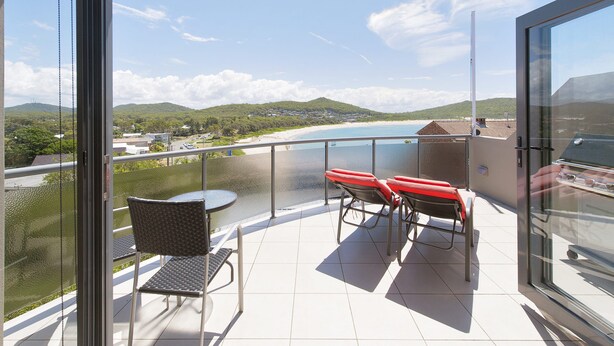 Un balcon avec une table et des chaises, donnant sur une plage et des collines.