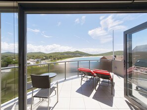 Un balcon avec une table et des chaises, donnant sur une plage et des collines.