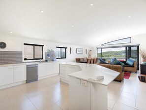 A modern kitchen with white cabinetry, a built-in dishwasher, and a large island with a phone. - Fingal Surf and Sand Pet Friendly with views (Fingal Bay)
