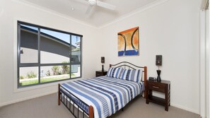 A bedroom with a large window, a bed with a striped bedspread, two bedside tables with lamps, and a ceiling fan. - Fingal Surf & Sand, 14A Pacific Drive- Modern, 2-storey duplex between bushland and the beach (Fingal Bay)