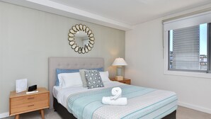 Quarto bem organizado com cama, mesas de cabeceira, abajur e janela.