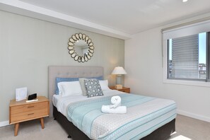 Een netjes opgemaakt slaapkamer met een bed, nachtkastjes, een lamp en een raam.