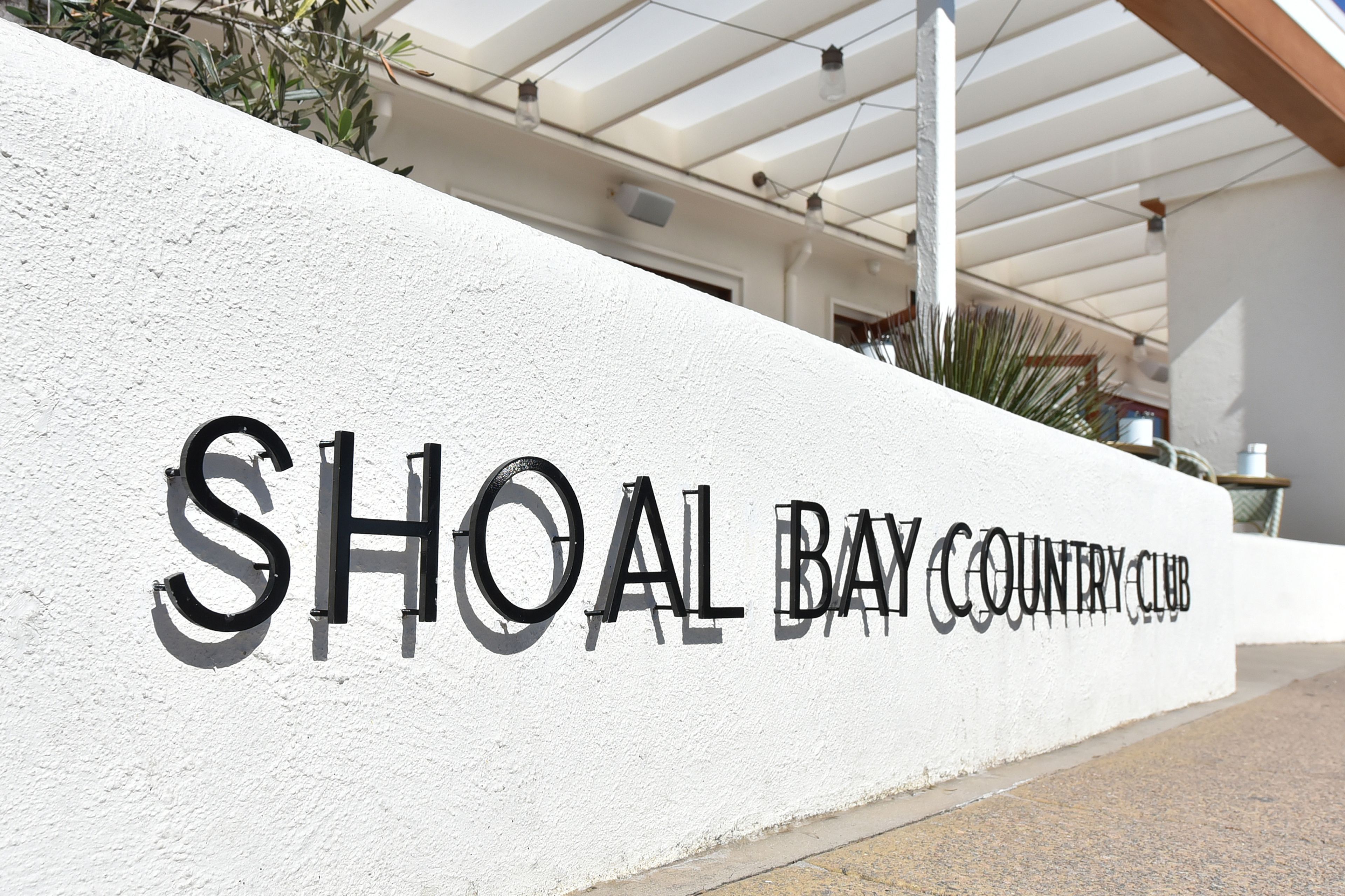 Een witte muur met de tekst 'SHOAL BAY COUNTRY CLUB' in zwarte letters.