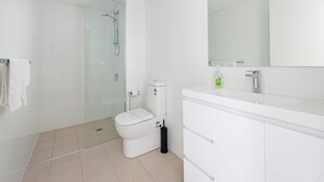 Casa de banho moderna com cabine de duche em vidro, sanita branca e toucador branco com espelho.