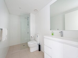 Een moderne badkamer met een douchecabine van glas, een wit toilet en een witte wastafel met spiegel.