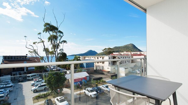 A balcony with a view of a parking lot, a building with a sign for a fish club, and a mountain in the background. - Sought after complex in Shoal Bay (Shoal Bay)