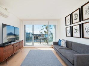 A modern living room with a flat-screen TV, a grey sofa, a wooden cabinet, and a patterned rug.